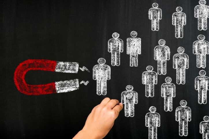 Magnet attracting illustrated people on a chalkboard, representing website leads and strategies for converting visitors into enquiries.